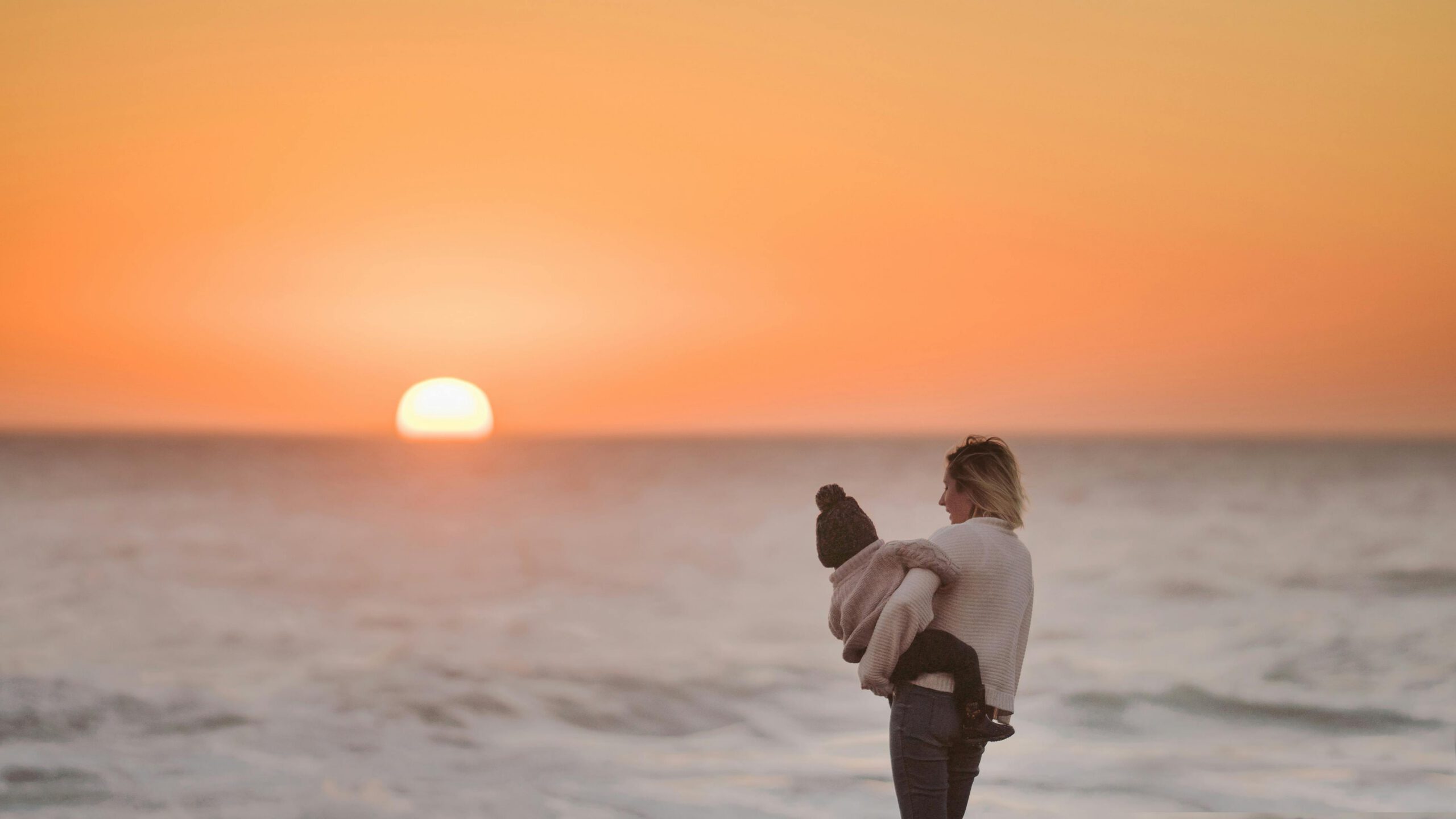 A woman holding her baby watching the sunset at a beach
