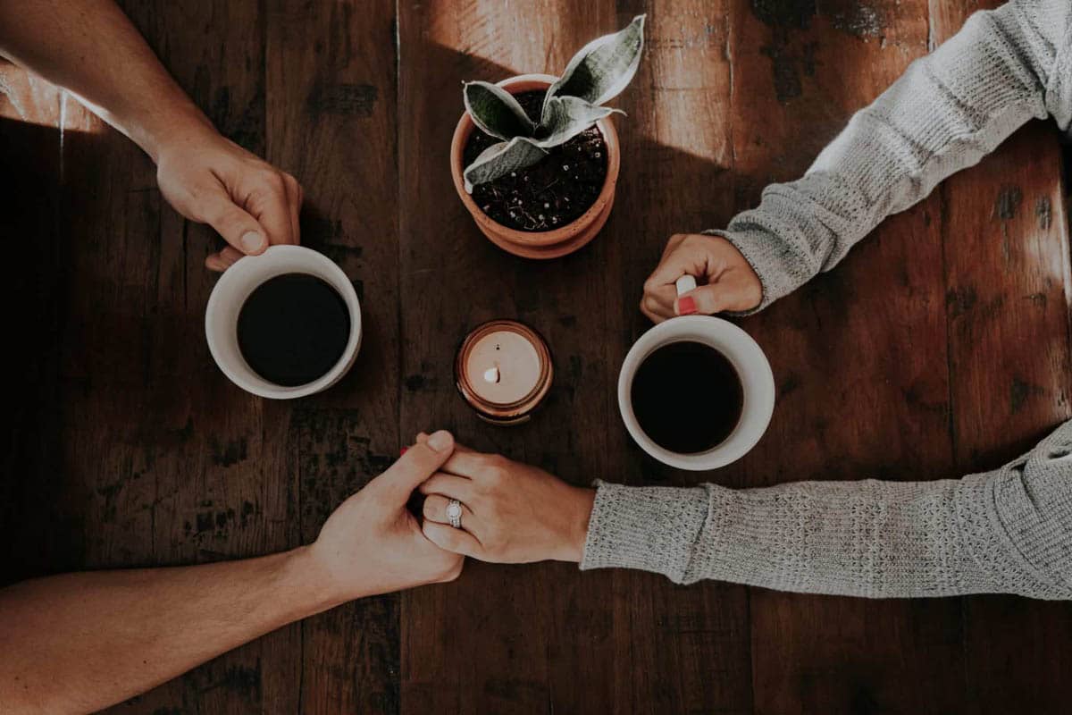 Spouses, husband and wife, holding hands while drinking coffee