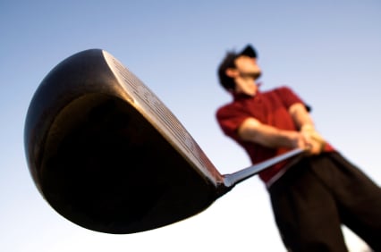 Camera angle under a golfer with the driver in main focus as the golfer looks into the distance before his shot