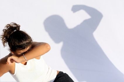Woman assault victim shielding her face and laying on the ground with a visible shadow of a man about to commit assault and hit her