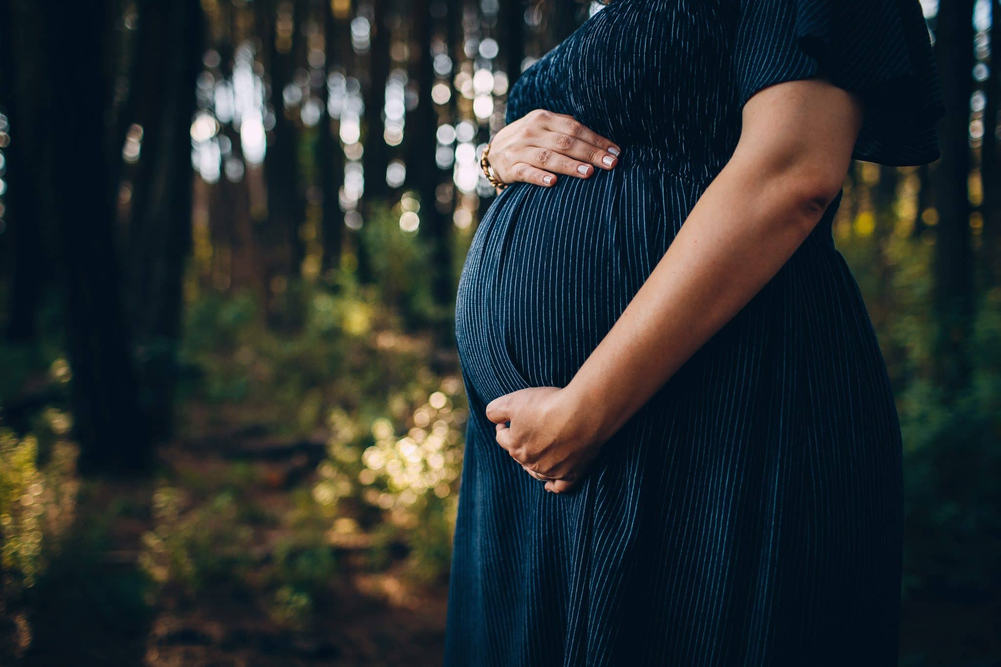A pregnant woman holding her stomach in the forest